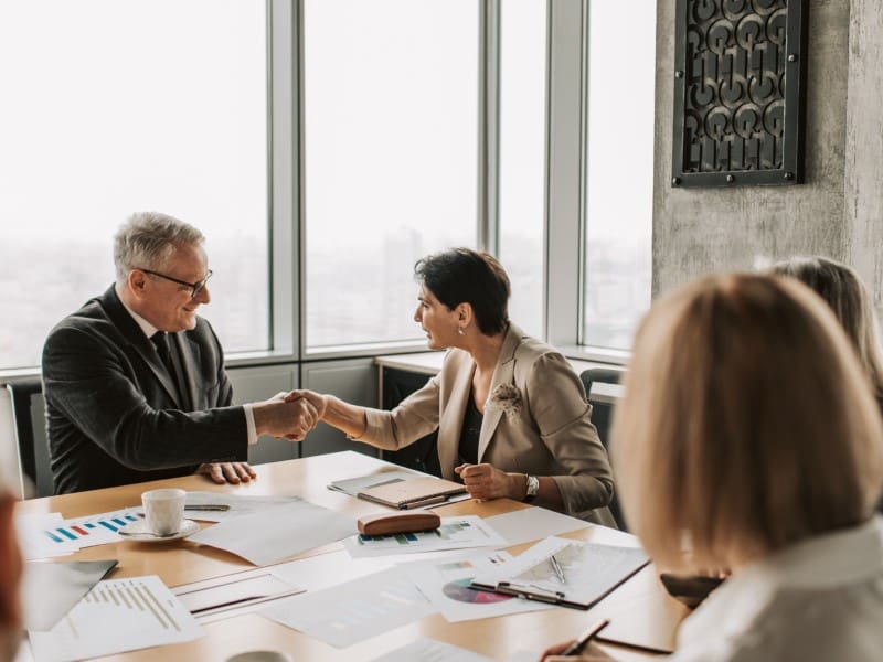 A man and woman shaking hands over a table.